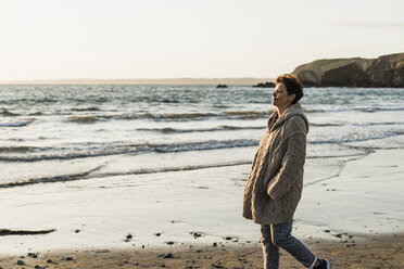 Frankreich, Halbinsel Crozon, Frau in Strickjacke am Strand bei Sonnenuntergang - UUF008333