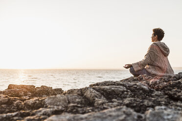 France, Crozon peninsula, woman meditating at beach at sunset - UUF008339