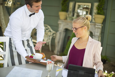 Kellner serviert einer Geschäftsfrau in einem Restaurant im Freien ein Dessert - ZEF010262