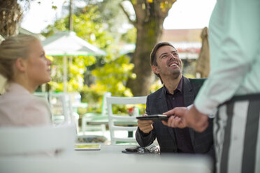 Customer handing over bill to waiter at outdoor restaraunt - ZEF010270