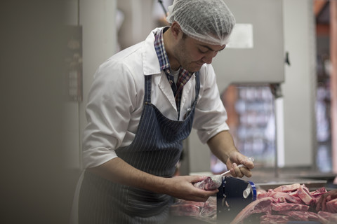 Metzger, der rohes Fleisch in der Metzgerei verpackt, lizenzfreies Stockfoto