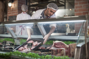 Butcher putting fresh meat on display in butchery - ZEF010338