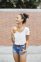 Happy young woman holding orange juice outdoors - MRAF000157