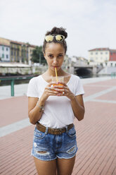 Young woman drinking orange juice on city square - MRAF000158