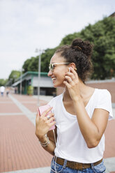 Happy young woman listening to music outdoors - MRAF000174