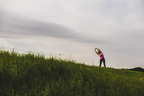 Sportliche junge Frau beim Stretching in ländlicher Landschaft - UUF008355
