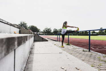 Junge Frau beim Dehnen in einem Leichtathletikstadion - UUF008368