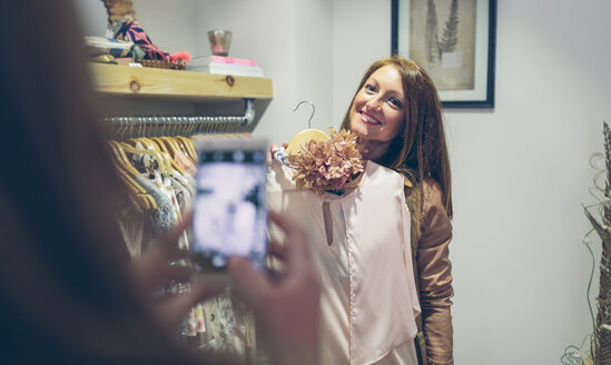 Woman taking picture of friend holding dress in a boutique - DAPF000316