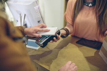 Frau beim Bezahlen mit einem Smartphone mit NFC-Technologie in einem Geschäft - DAPF000330