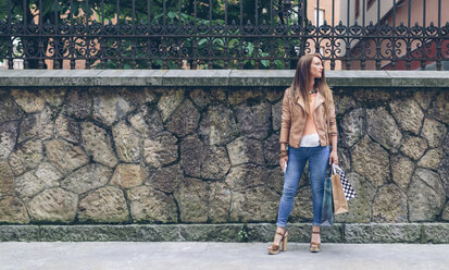 Woman holding shopping bags standing in front of stone wall - DAPF000335