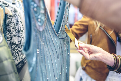 Close-up of woman checking price tag of a dress in a boutique - DAPF000352