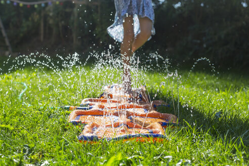 Mädchen springt auf aufblasbarem Wasserkissen im Garten, Teilansicht - SARF002859