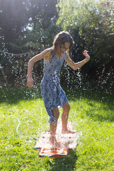 Mädchen hat Spaß mit aufblasbarem Wasserkissen im Garten - SARF002862