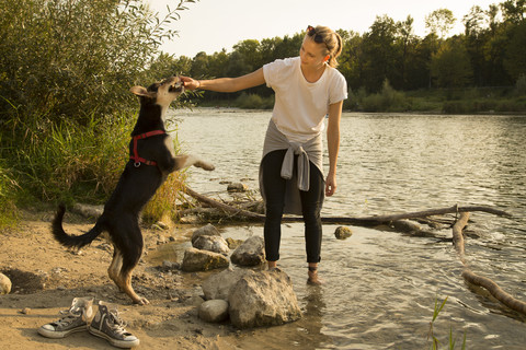 Young woman playing with her dog at riverside stock photo