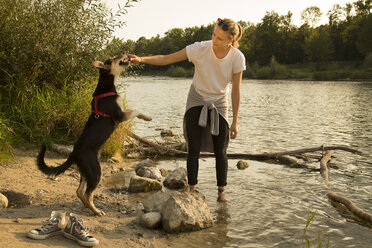 Junge Frau spielt mit ihrem Hund am Flussufer - FCF001070