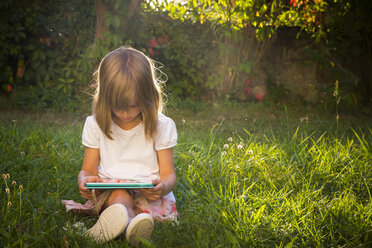 Kleines Mädchen sitzt auf einer Wiese und schaut auf eine Tafel - LVF005282