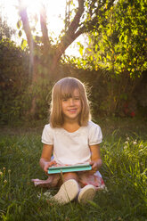 Porträt eines lächelnden kleinen Mädchens, das mit einem Tablet auf einer Wiese sitzt - LVF005283
