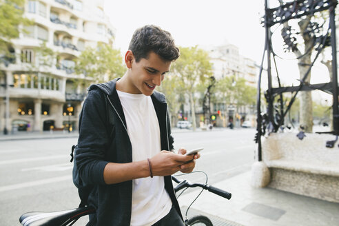 Jugendlicher mit einem Fahrrad in der Stadt, der sein Smartphone benutzt - EBSF001729