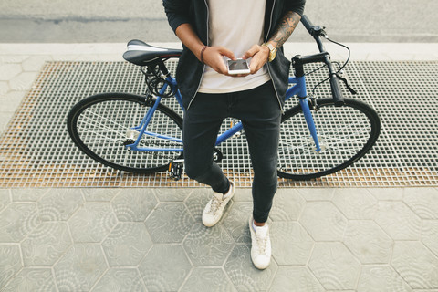 Jugendlicher mit einem Fahrrad in der Stadt, der sein Smartphone benutzt, lizenzfreies Stockfoto