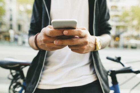 Jugendlicher mit einem Fahrrad in der Stadt, der sein Smartphone benutzt - EBSF001731