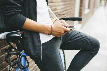 Jugendlicher mit einem Fahrrad in der Stadt, der sein Smartphone benutzt - EBSF001747