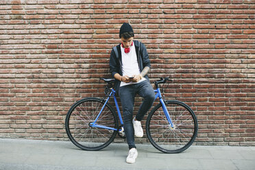 Teenager mit Fixie-Fahrrad, der ein Smartphone benutzt - EBSF001750