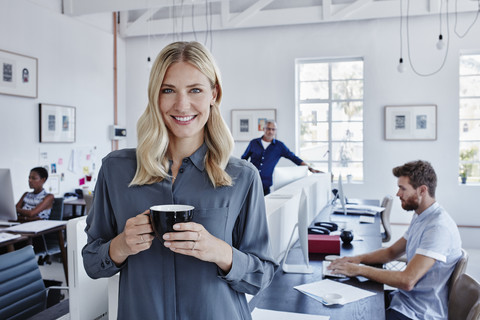 Porträt einer lächelnden Geschäftsfrau im Büro mit Mitarbeitern im Hintergrund, lizenzfreies Stockfoto