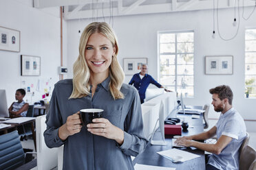 Portrait of smiling businesswoman in office with staff in background - RORF00290