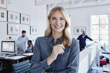 Portrait of smiling businesswoman in office with staff in background - RORF00293
