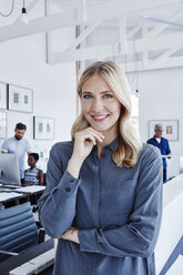 Porträt einer lächelnden Geschäftsfrau im Büro mit Mitarbeitern im Hintergrund - RORF00294