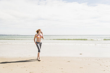 Teenager-Mädchen mit Handy auf dem Strand spazieren - UUF08399