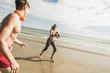 Teenager-Mädchen und junger Mann spielen mit einem Ball am Strand - UUF08415
