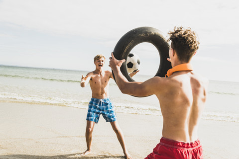 Zwei Freunde spielen mit einem Ball und einem Reifen am Strand, lizenzfreies Stockfoto