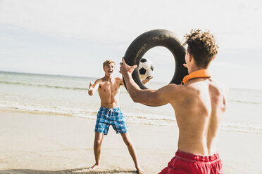 Zwei Freunde spielen mit einem Ball und einem Reifen am Strand - UUF08417