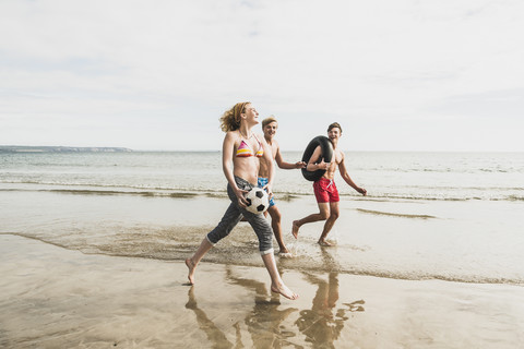 Freunde, die mit einem Ball und einem Reifen am Strand spazieren gehen, lizenzfreies Stockfoto