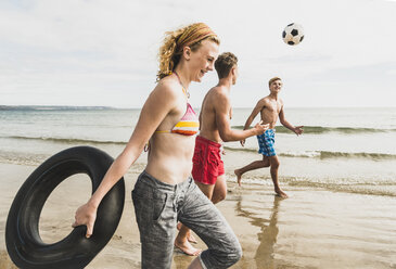 Freunde, die mit einem Ball und einem Reifen am Strand spazieren gehen - UUF08420