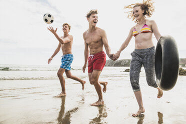 Freunde laufen mit einem Ball und einem Reifen am Strand - UUF08421