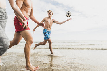 Freunde laufen mit einem Ball und einem Reifen am Strand - UUF08422