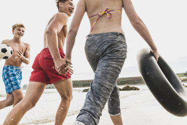 Friends running with a ball and tyre on the beach - UUF08423