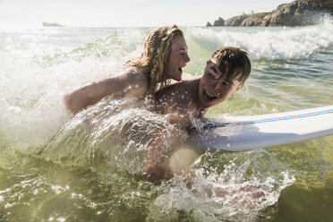 Teenage couple having fun on surfboard in the sea - UUF08435