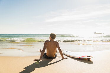 Teenage boy sitting on surfboard at the sea - UUF08443