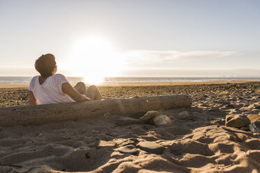 Frankreich, Bretagne, Halbinsel Crozon, Frau sitzt bei Sonnenuntergang am Strand - UUF08471