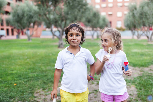 Kleines Mädchen und Junge mit Seifenblasenringen in einem Park - VABF00774