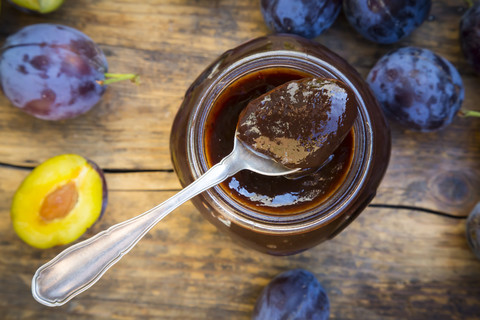 Teelöffel mit Pflaumenmarmelade auf Einmachglas und Pflaumen auf Holz, lizenzfreies Stockfoto