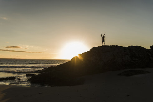 Frankreich, Halbinsel Crozon, junger Mann auf Felsen bei Sonnenuntergang - UUF08485