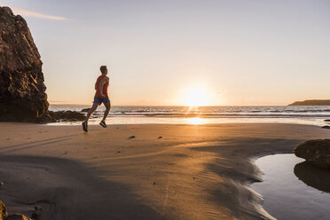 Frankreich, Halbinsel Crozon, Jogger am Strand bei Sonnenuntergang - UUF08495