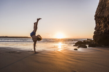 France, crozon peninsula, young man doing handstand on one arm at sunset - UUF08498