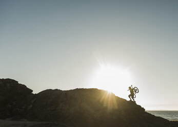 France, crozon peninsula, mountainbiker carrying his bike at sunset - UUF08507
