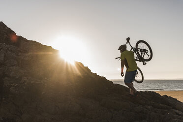 Frankreich, Halbinsel Crozon, Mountainbiker mit Fahrrad bei Sonnenuntergang - UUF08511
