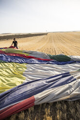 Man packing up a hot air balloon envelope in field - ABZF01240